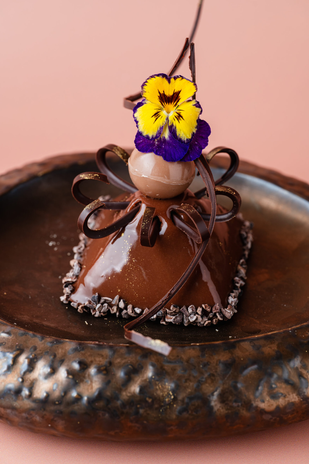 Chocoladepiramide met een paarse eetbare bloem op een bronzen bord